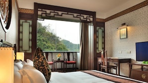 A hotel room with a large bed, a desk, a chair, a TV, and a view of the outdoors. - Guilin Park Hotel (Guilin)