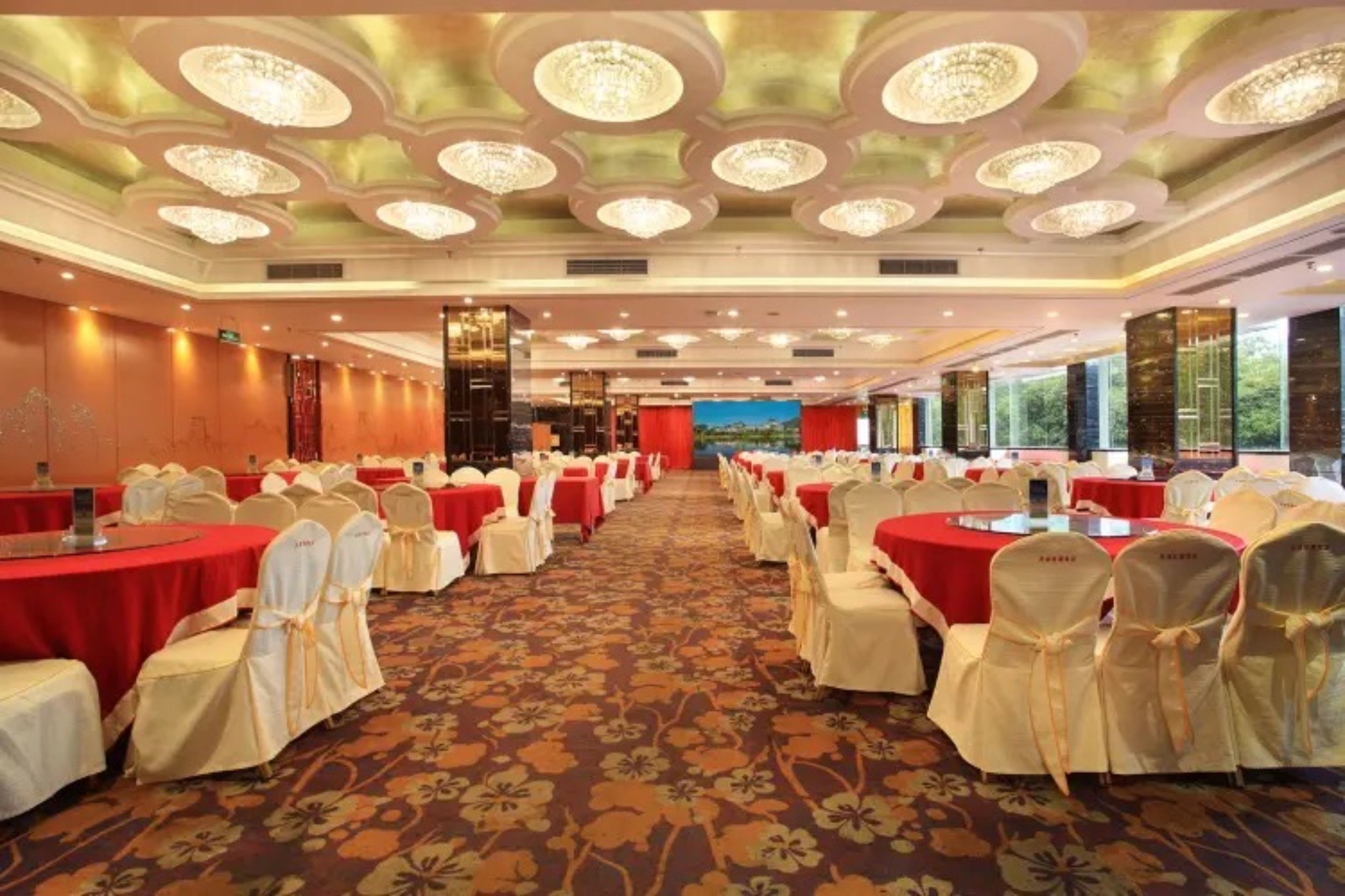 A banquet hall with round tables, white chairs, and red tablecloths.