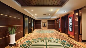 A hotel corridor with a patterned carpet, wooden paneling, and a potted plant. - Guilin Park Hotel (Guilin)