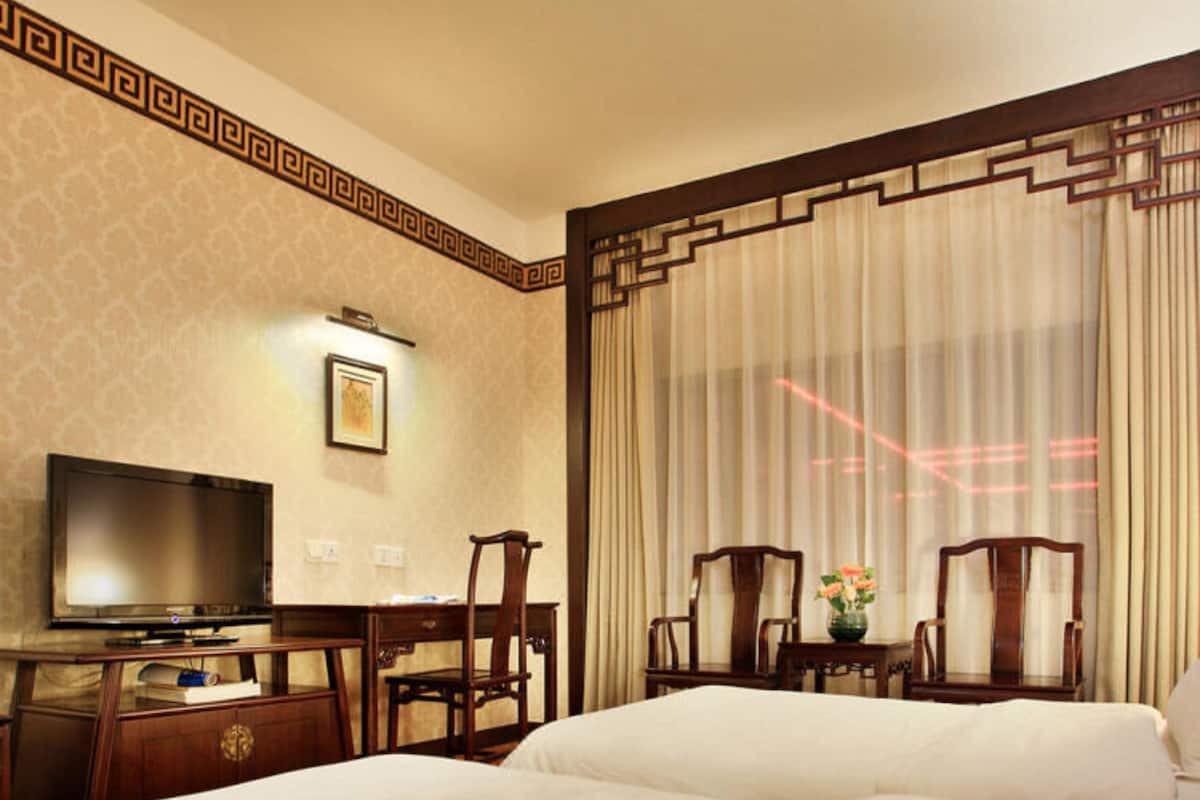 A hotel room with a bed, a desk with a television, and two chairs.