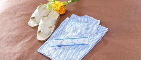 A pair of white sandals, a blue checkered cloth, and a small bouquet of yellow flowers on a brown surface.