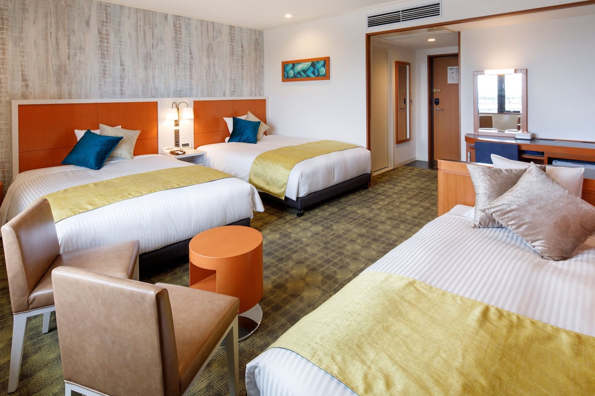 A hotel room with two beds, a desk, a chair, and a small table.