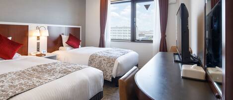 A hotel room with two beds, a desk, a chair, a TV, and a window with curtains.