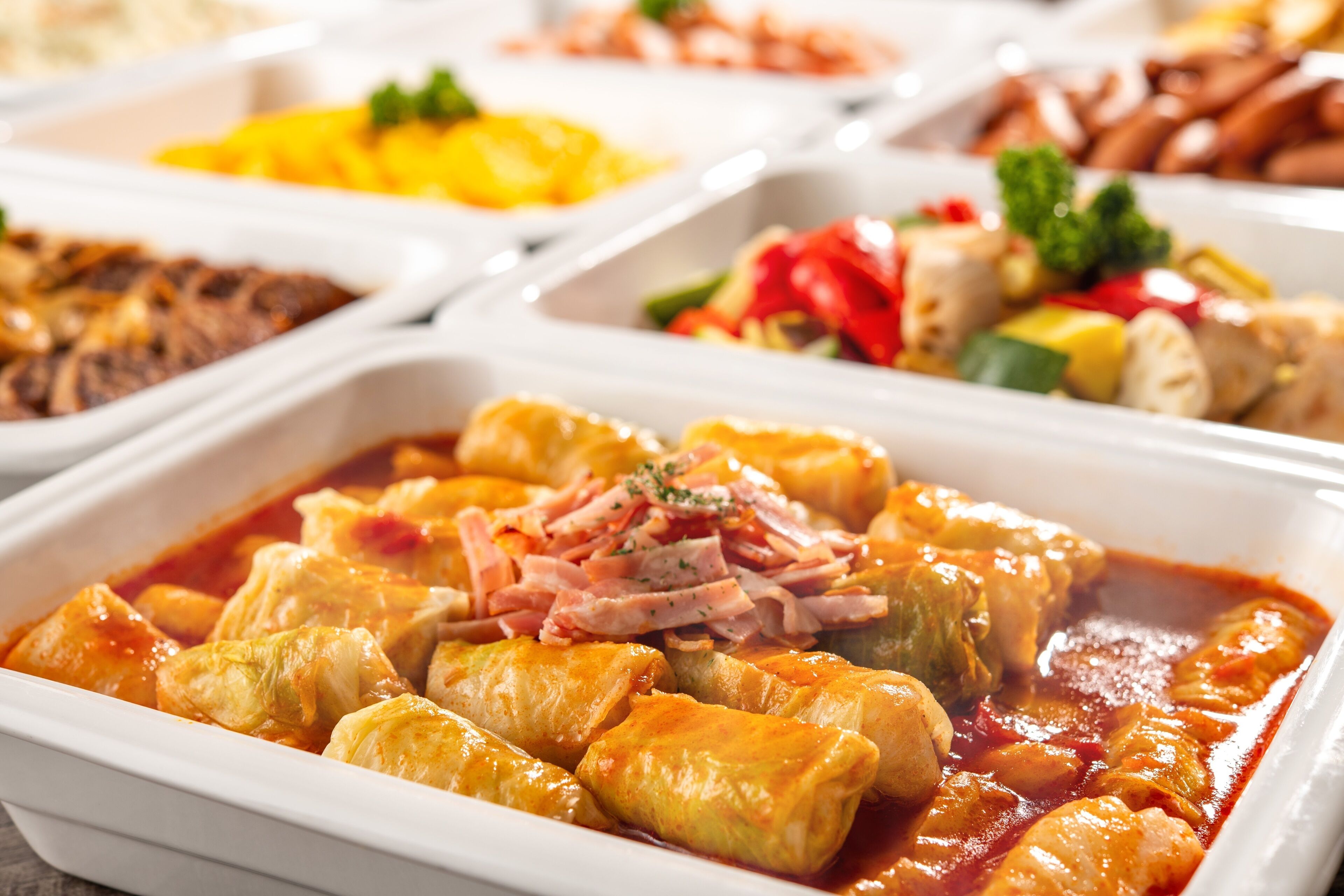 A buffet with various dishes including stuffed cabbage rolls in tomato sauce.