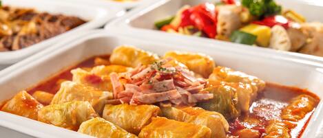 A buffet with various dishes including stuffed cabbage rolls in tomato sauce.