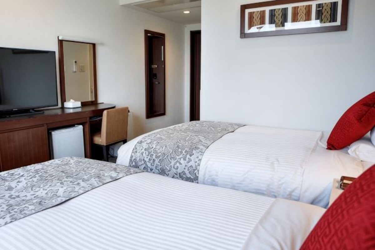 A hotel room with two beds, a desk with a television, and a mirror.