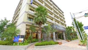 Un hotel de varios pisos con un diseño moderno, que cuenta con balcones, una entrada central y jardines ajardinados.