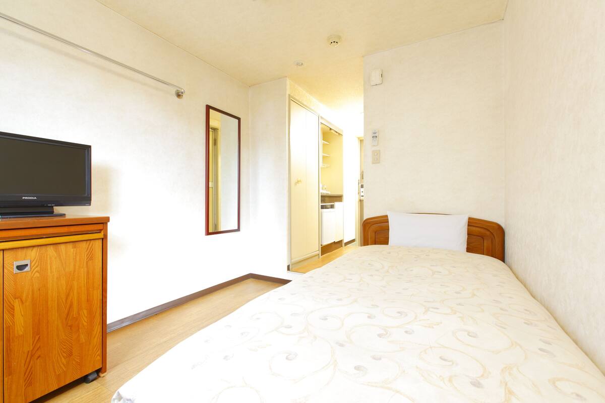 A hotel room with a bed, a wooden cabinet, a television, and a bathroom visible through an open door.