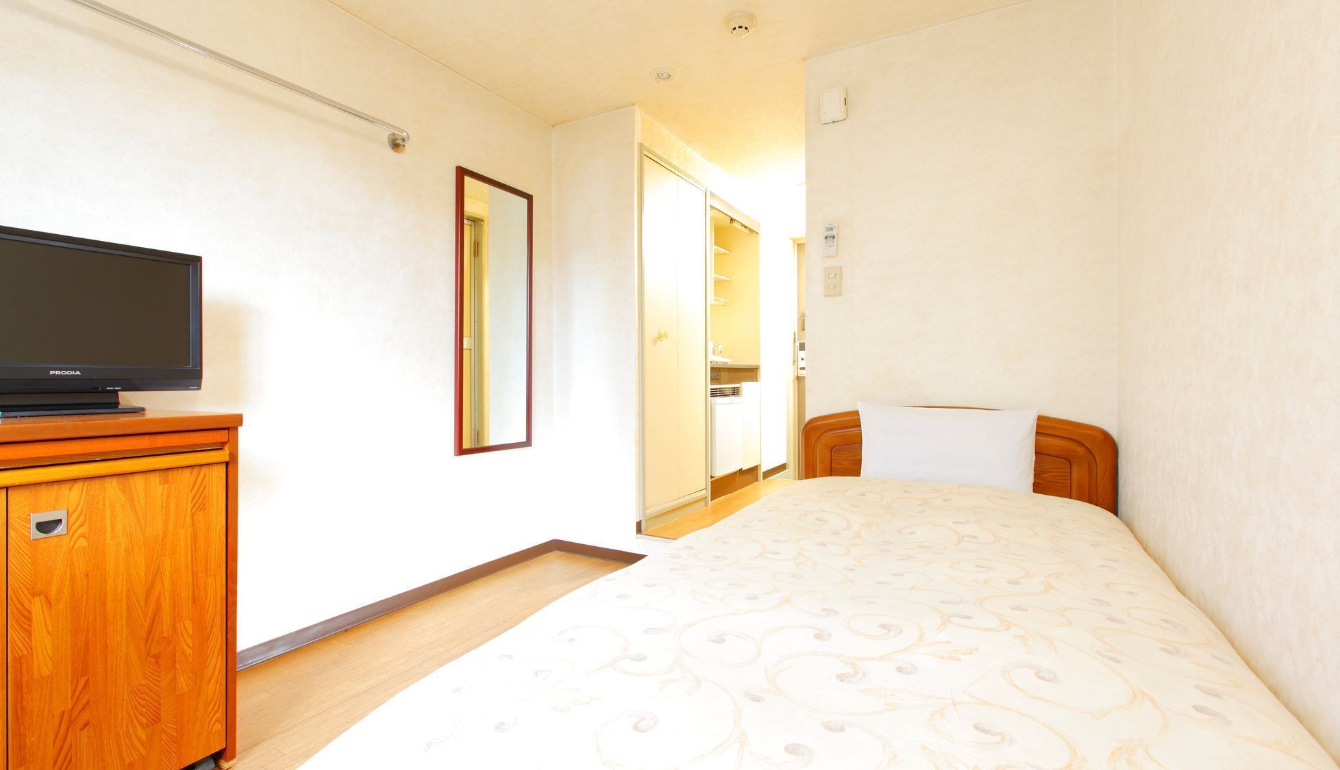 A hotel room with a bed, a TV on a wooden cabinet, a mirror, and a wardrobe.