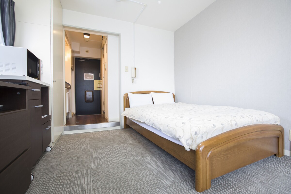 A bedroom with a bed, a dresser, a microwave, and a door leading to another room.