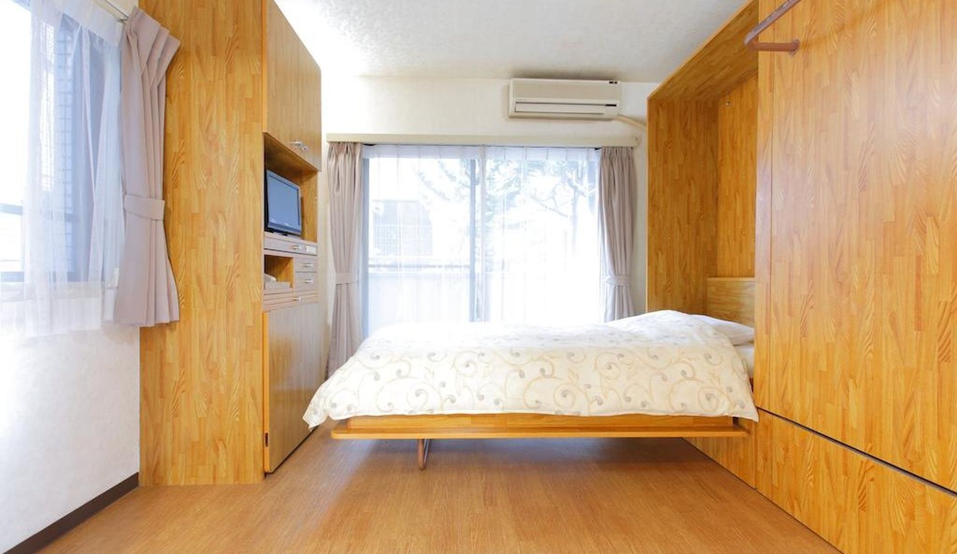 A room with a bed, wooden walls, a TV, and an air conditioning unit.