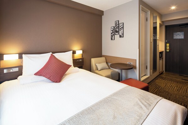Une chambre d’hôtel avec un grand lit, deux tables de chevet avec des lampes, une petite table ronde, une chaise et une porte dotée d’un miroir.