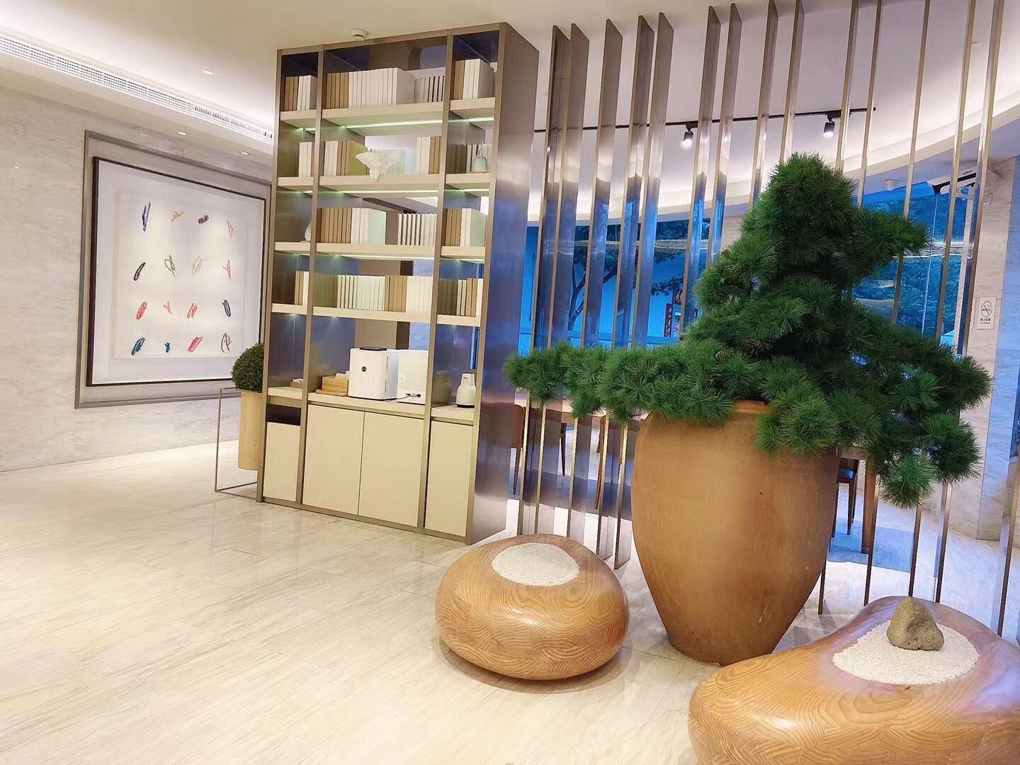 A modern interior with a bookshelf, a large potted plant, and two wooden stools.