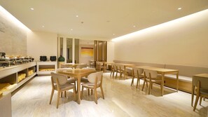 Un comedor moderno con mesas y sillas de madera, una barra de buffet con platos cubiertos y un espejo grande.