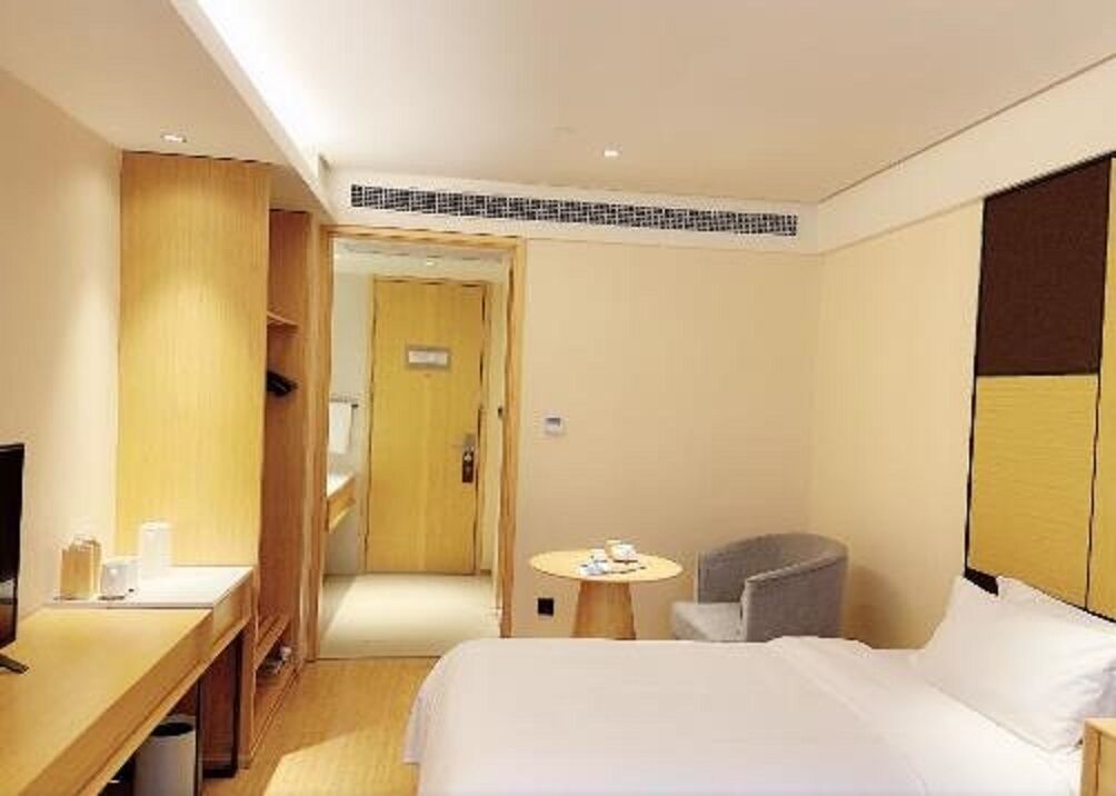 A hotel room with a bed, a desk, a chair, a small table, and a wardrobe.