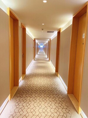 Un pasillo de hotel con pisos alfombrados, puertas de madera e iluminación empotrada.