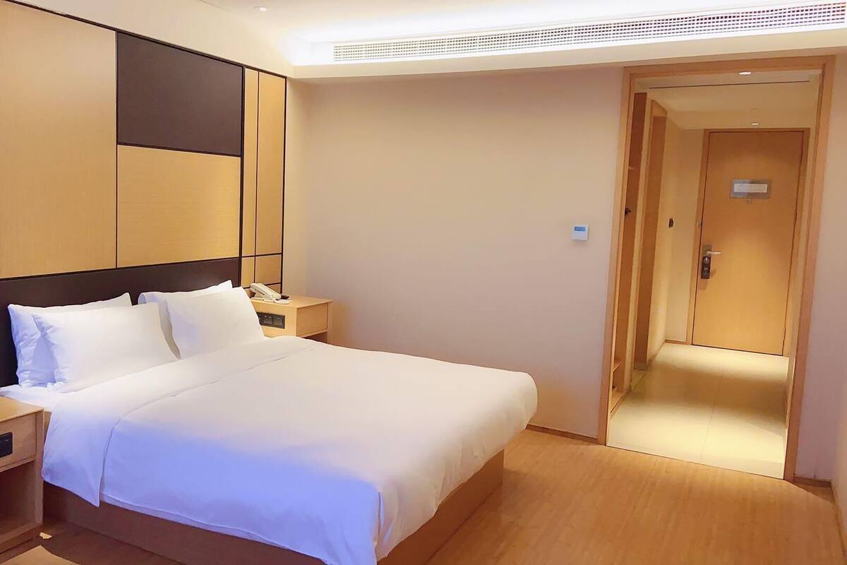 Une chambre d’hôtel avec un grand lit, des tables de chevet, un téléphone et une porte donnant sur une autre pièce.