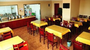 Un restaurant avec plusieurs tables et chaises, un comptoir équipé de matériel de cuisine et un téléviseur accroché au mur.