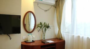 A hotel room with a flat-screen TV, a wooden desk with a white kettle, a mirror, and a potted plant. - Greentree Inn Tianjin Dongli Development Zone Expr (Tianjin)
