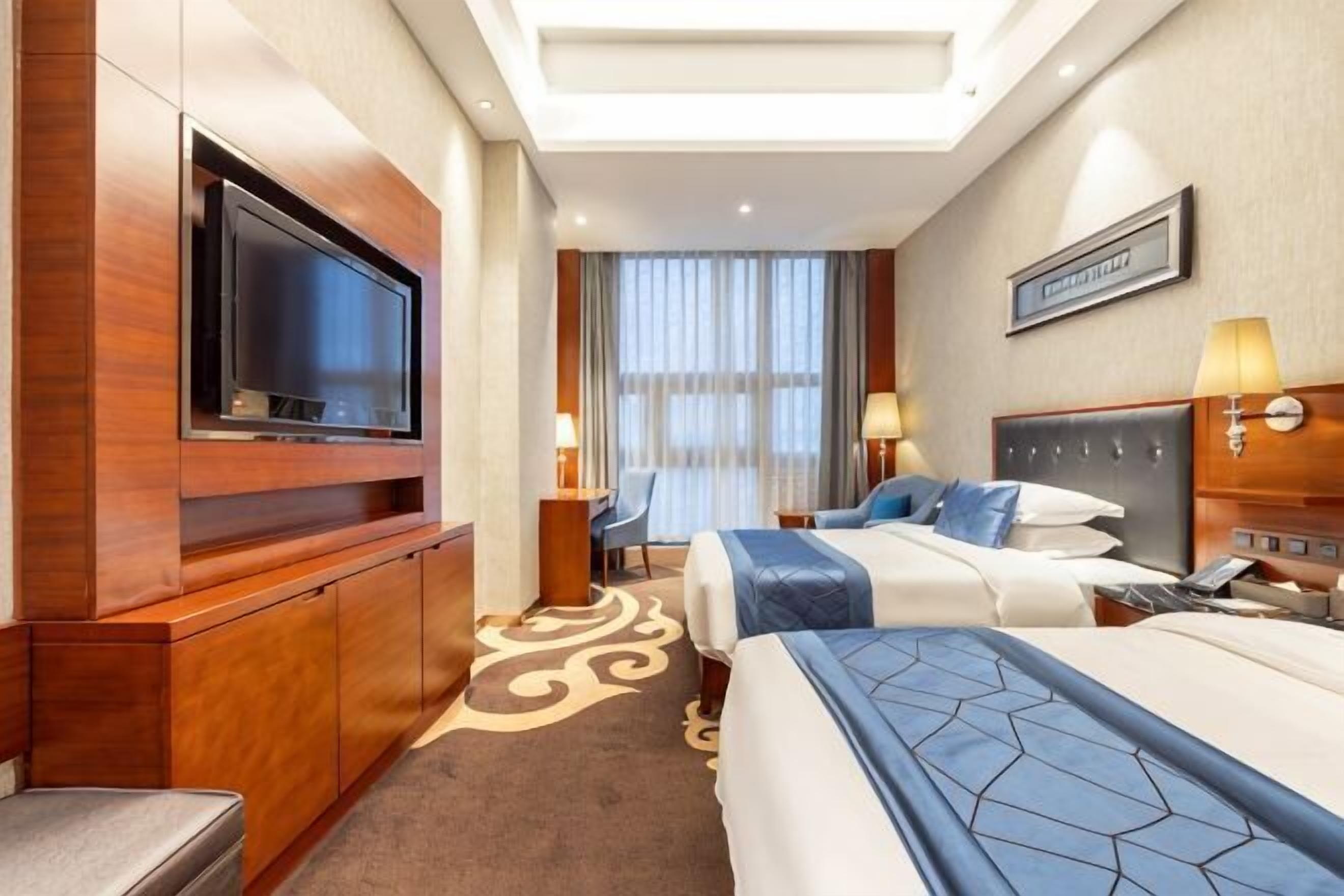 A hotel room with a television, two beds, a desk, and a window with curtains.