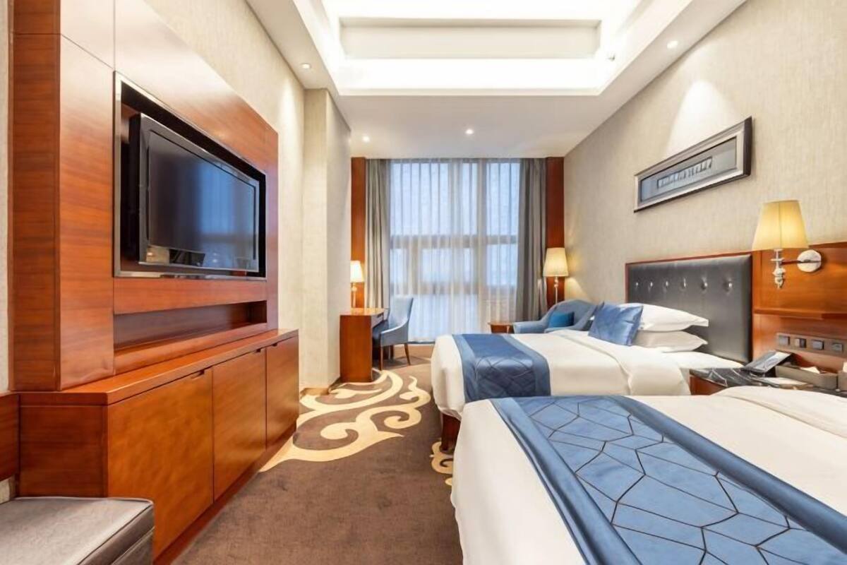 A hotel room with a television, two beds, a desk, and a window with curtains.