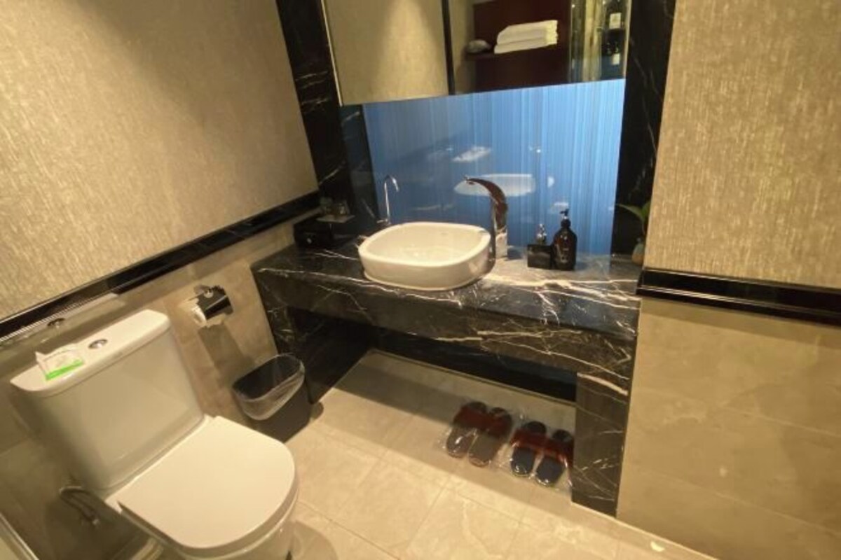 A modern bathroom with a white toilet, a sink with a marble countertop, and a mirror above the sink.