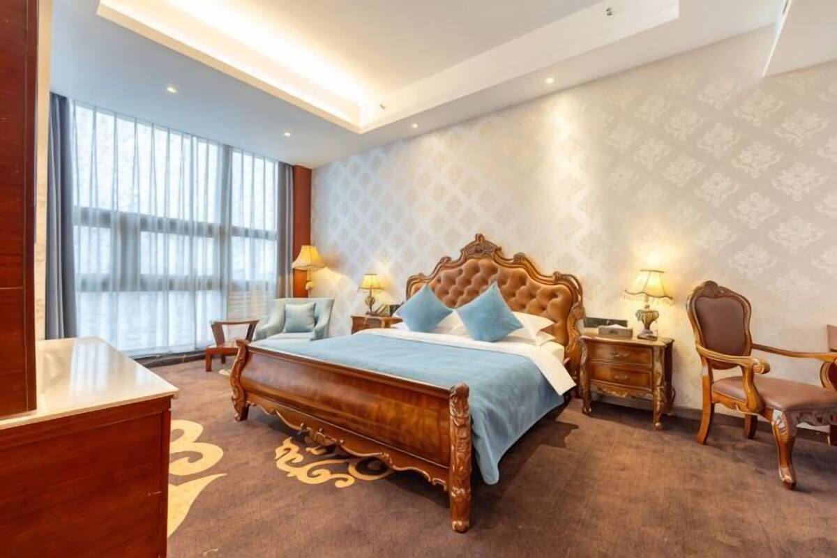 A hotel room with a large bed, two bedside tables, a chair, a desk, and a large window.