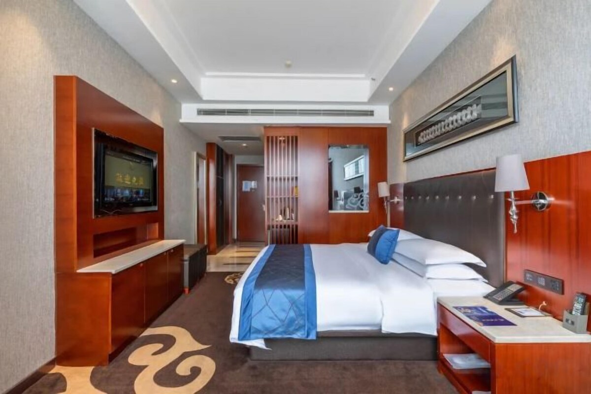 A hotel room with a bed, TV, bedside table, and a mirror.