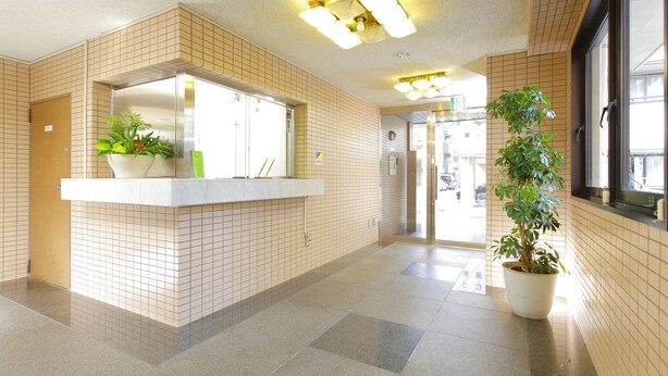 A reception area with a tiled floor, a reception desk with a potted plant, and a large window on the right. - Flexstay Inn Tamagawa (Kawasaki)