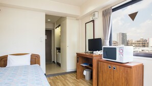 A hotel room with a bed, a desk with a computer and a microwave, a window with a city view, and a trash bin. - Flexstay Inn Tamagawa (Kawasaki)