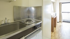 A modern kitchen with a stainless steel stove, a built-in oven, and a sink. There is a wooden cabinet and a window with curtains. - Flexstay Inn Tamagawa (Kawasaki)