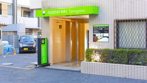 The entrance to FLEXSTAY INN Tamagawa with a tiled facade, a visible reception desk, and a parking area in the foreground. - Flexstay Inn Tamagawa (Kawasaki)