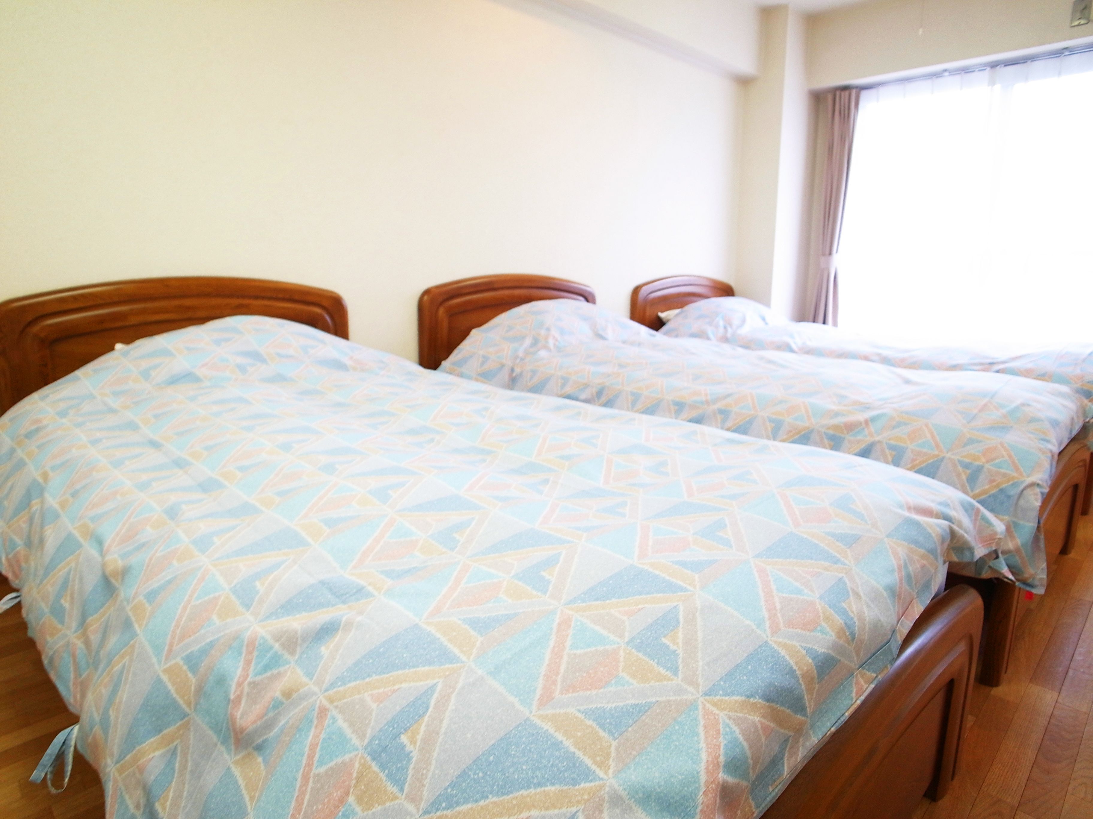 A room with two wooden beds with geometric patterned bedding, a wooden floor, and a window with curtains.