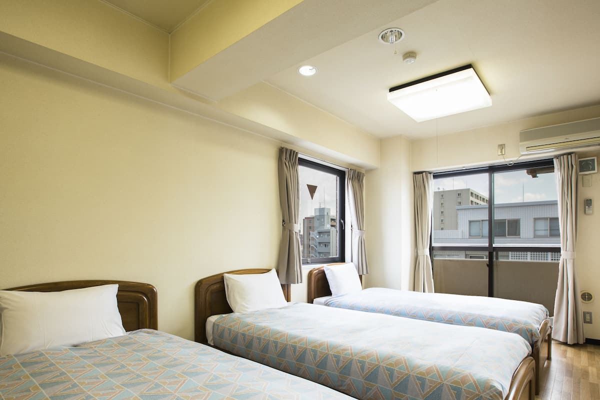 A hotel room with two beds, a window with curtains, a ceiling light, and an air conditioning unit.