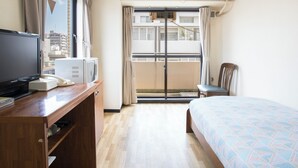 A hotel room with a bed, a desk with a TV, a phone, and a microwave. There is a chair and a window with curtains. - Flexstay Inn Tamagawa (Kawasaki)
