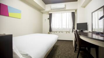 A hotel room with a bed, a desk, a chair, a TV, and an air conditioning unit.