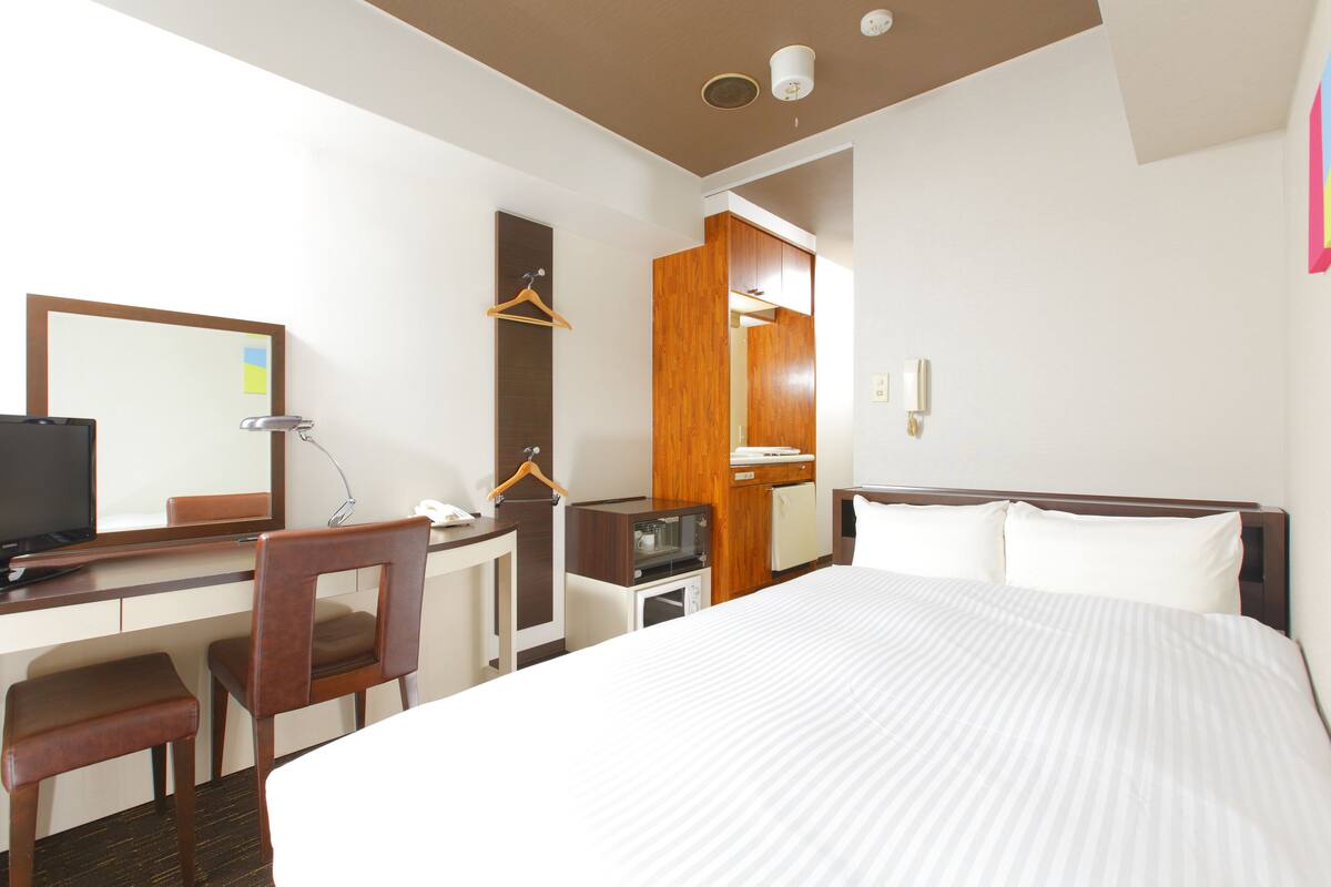 Une chambre d’hôtel équipée d’un lit, d’un bureau, d’une chaise, d’une télévision, d’une armoire et d’un miroir.