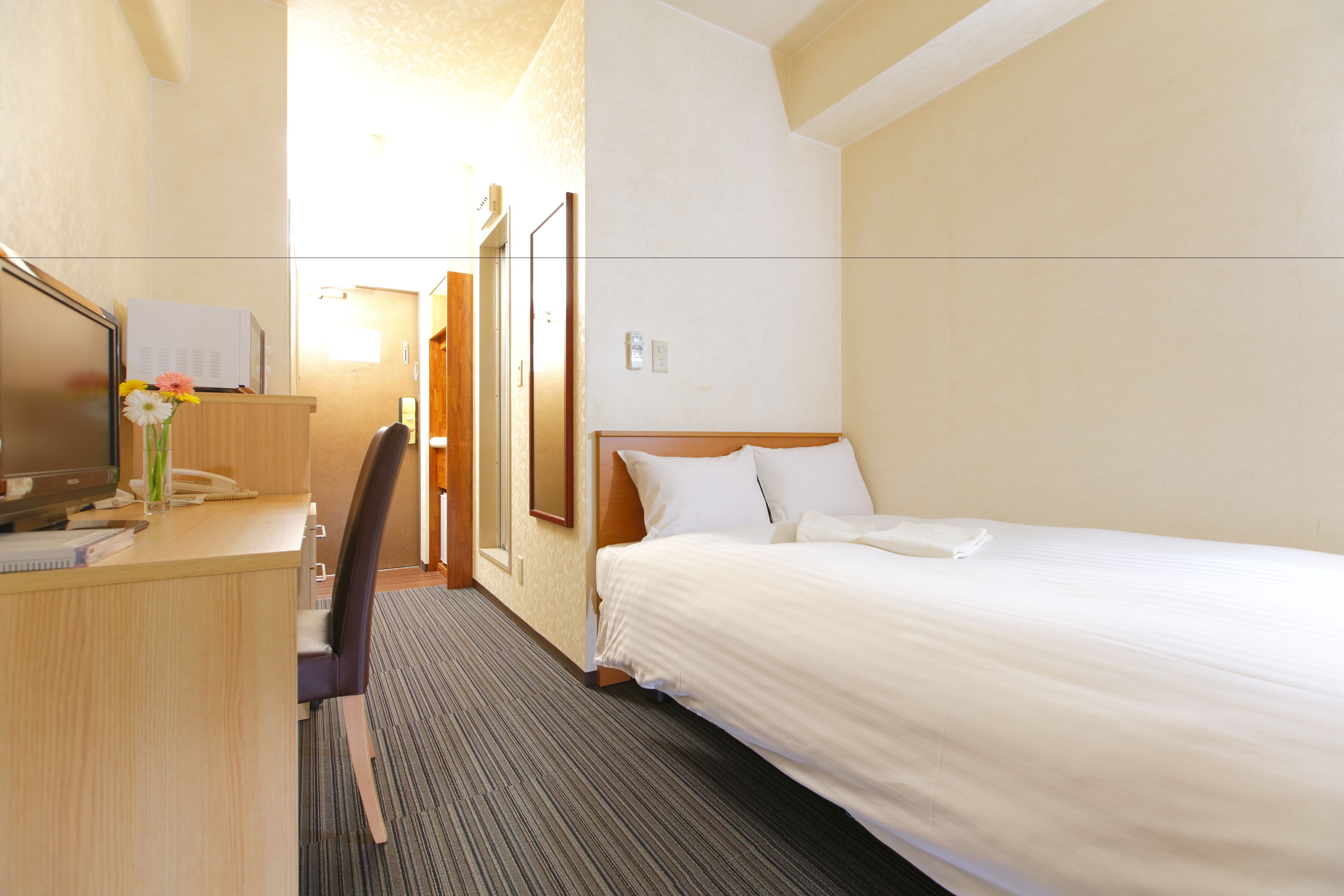 Une chambre d’hôtel comprenant un lit, un bureau avec un ordinateur et un téléphone, une chaise et une petite table sur laquelle est posé un vase de fleurs.