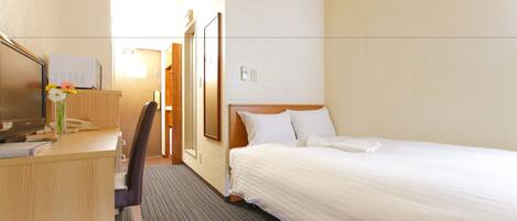 A hotel room with a bed, a desk with a computer and a telephone, a chair, and a small table with a vase of flowers.