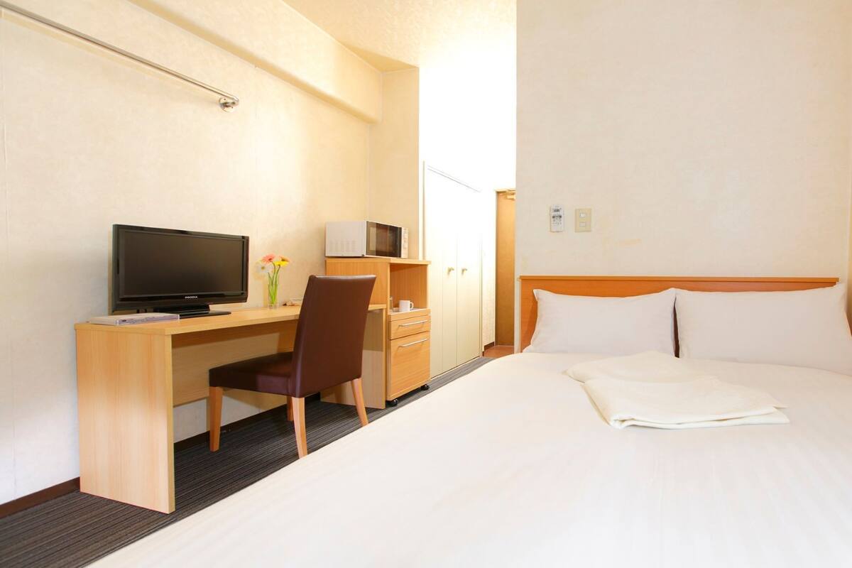 Une chambre d’hôtel équipée d’un lit, d’un bureau avec une télévision, d’une chaise, d’un four à micro-ondes et d’une armoire.