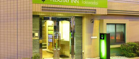 The exterior of the FLEXSTAY INN in Tokiwaidai with a green sign, glass doors, and a small garden area.