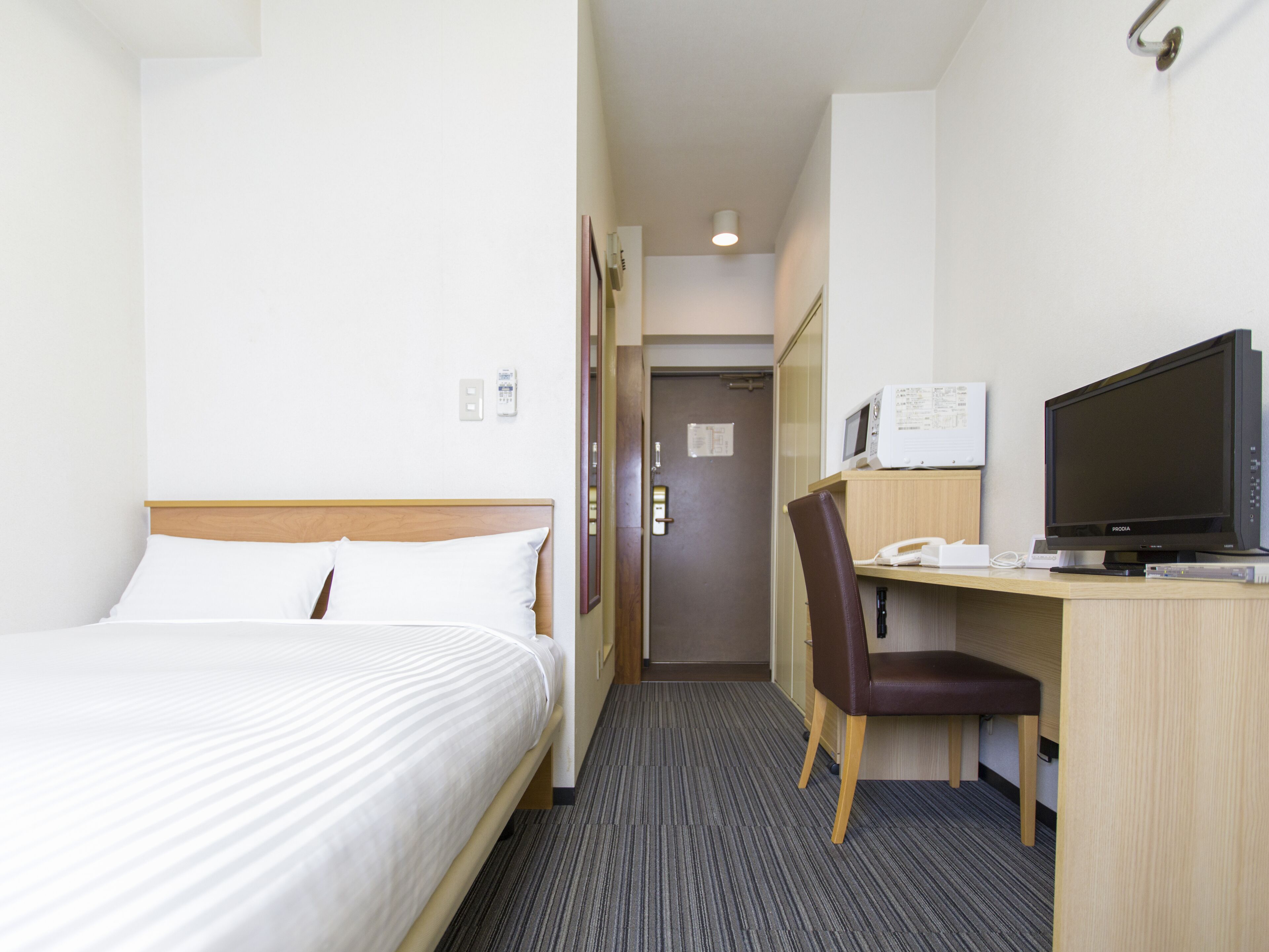 Ein Hotelzimmer mit einem Bett, einem Schreibtisch mit Fernseher und einem Sessel.