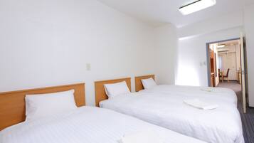 Habitación de hotel con dos camas, cabecero de madera, ropa de cama blanca y una lámpara en el techo.
