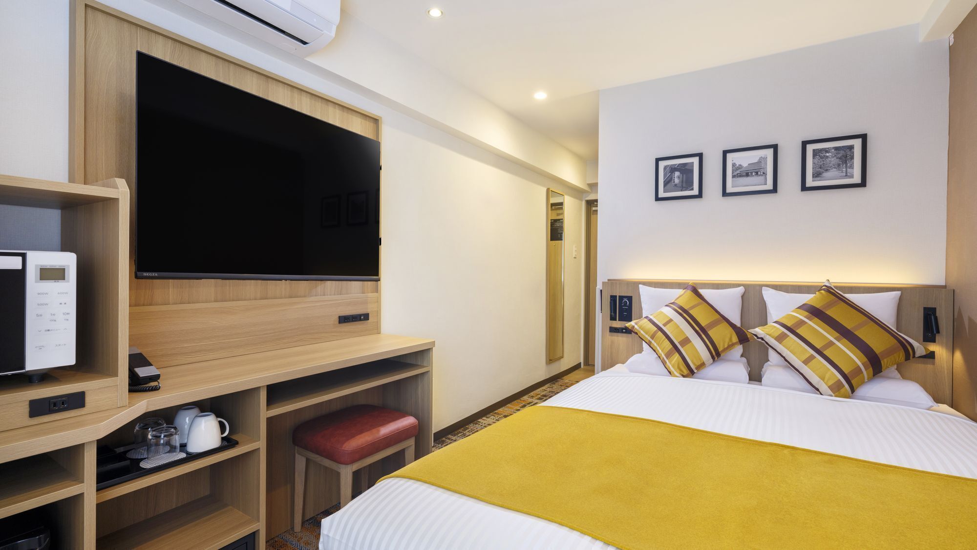 Habitació d'hotel amb un llit, una televisió, un microones, una taula petita amb una tetera i una panxa vermella.