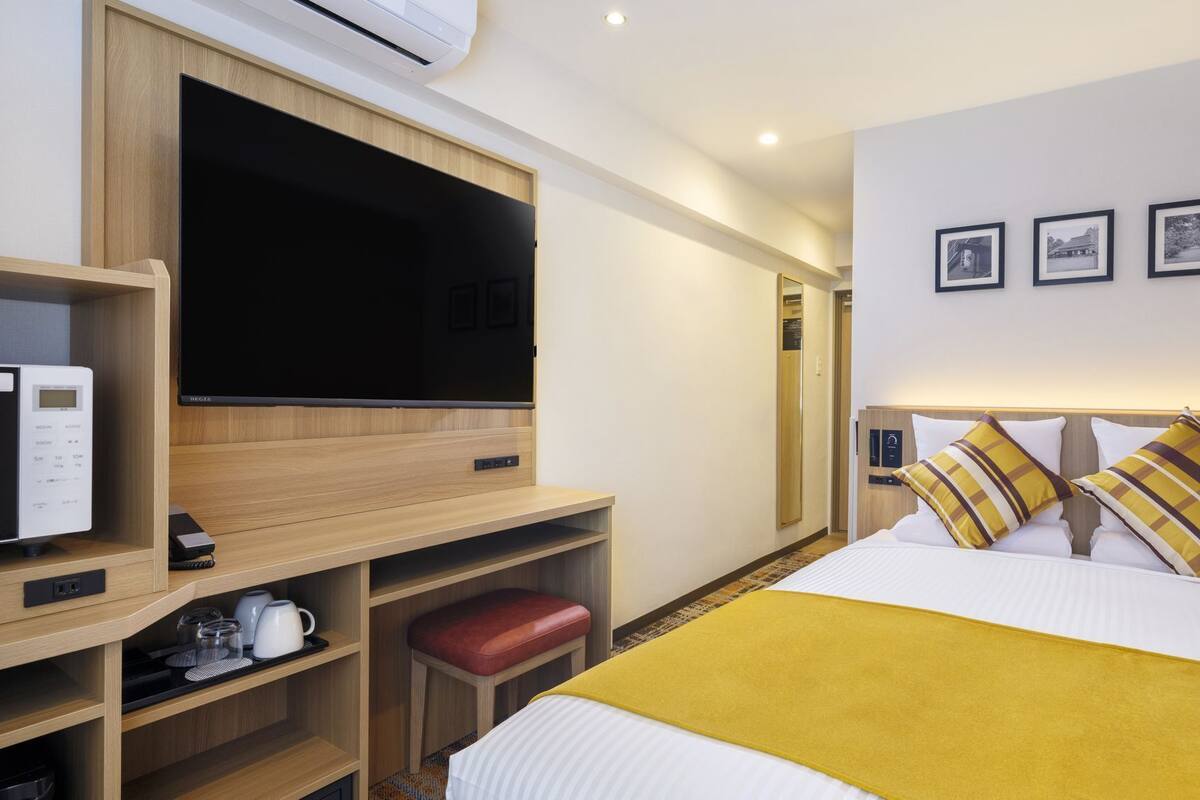 Ein Hotelzimmer mit Bett, Fernseher, Mikrowelle, einem kleinen Tisch mit Wasserkocher und einer roten Bank.