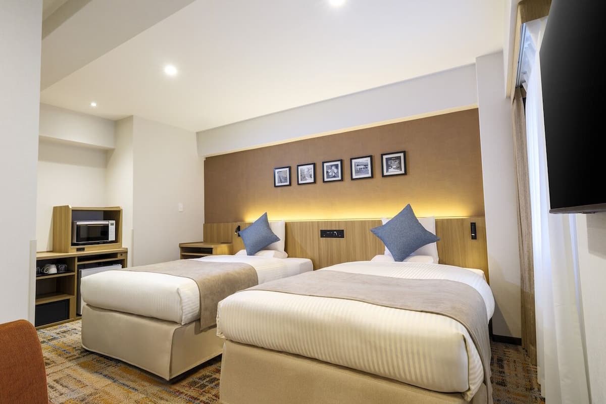 Une chambre d’hôtel avec deux lits, un four à micro-ondes, une télévision et un petit bureau.