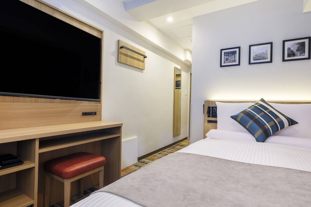Ein Hotelzimmer mit Bett, Schreibtisch mit Stuhl, Fernseher und Kleiderschrank.