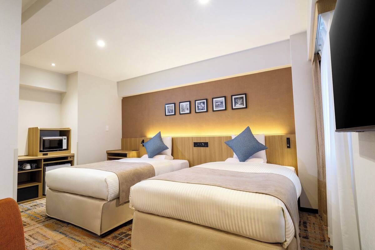 Ein Hotelzimmer mit zwei Betten, einer Mikrowelle, einem Fernseher und einem kleinen Schreibtisch.