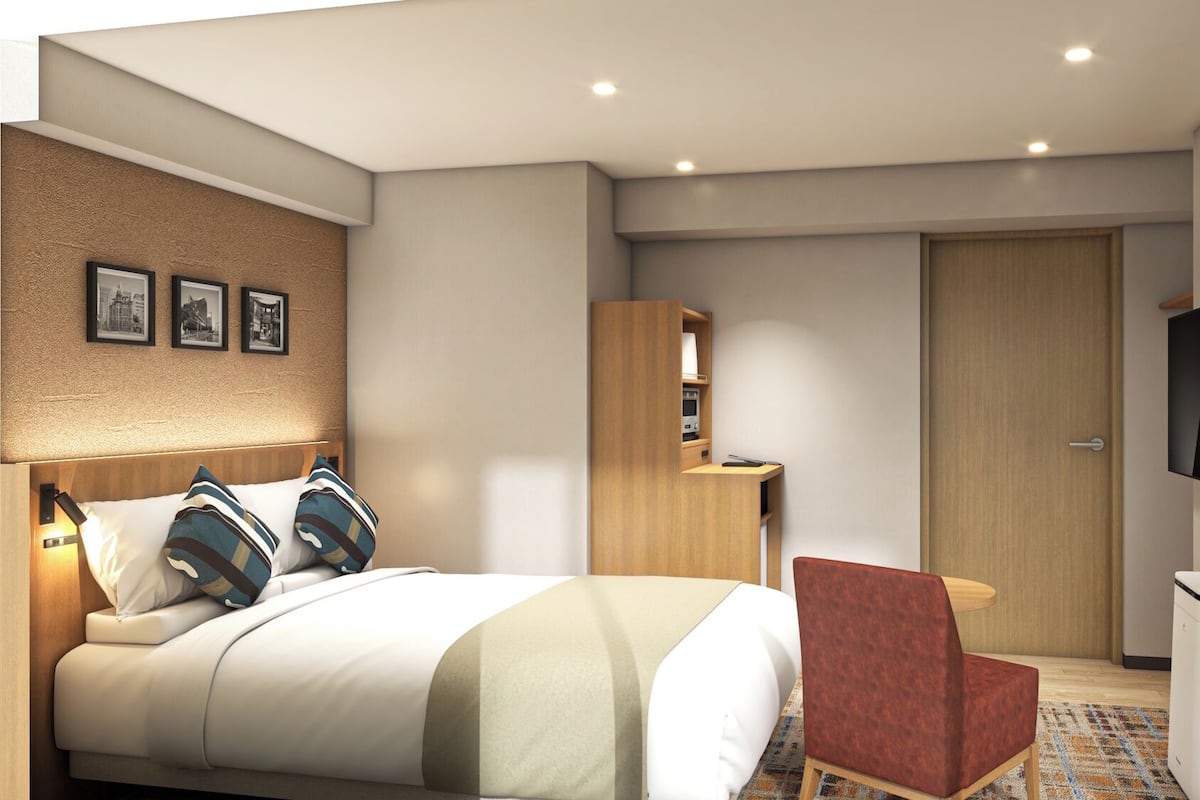 Une chambre d’hôtel moderne équipée d’un lit, d’un bureau, d’une chaise, d’une armoire, d’une télévision et d’une poubelle.