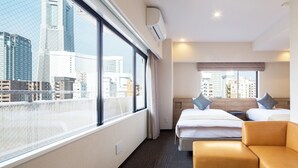 A hotel room with a large window, two beds, a sofa, and a view of the cityscape. - Flexstay Inn Sakuragicho (Yokohama)
